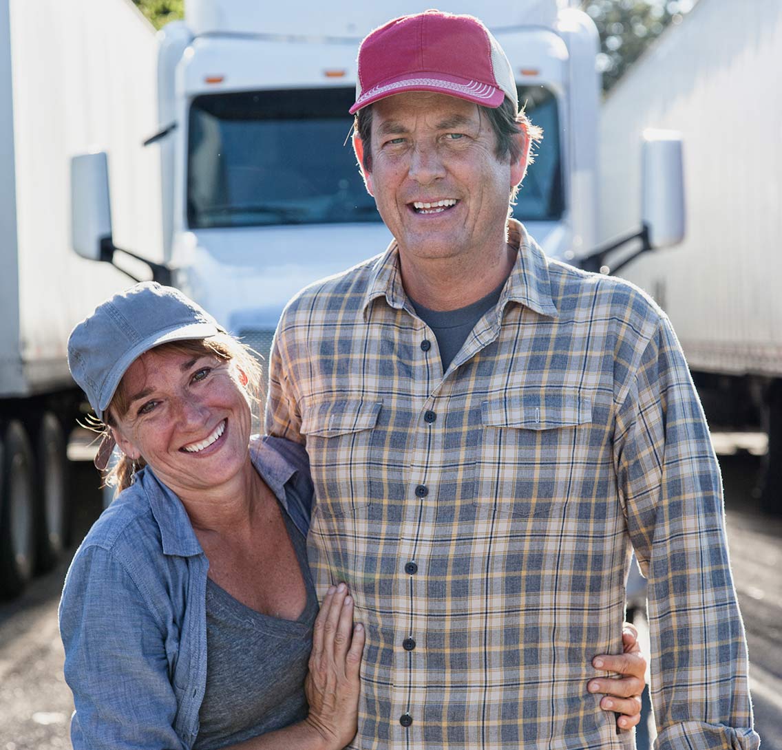 Two smiling truck drivers standing together in front of commercial trucks for LeCoop Truck and Trailer